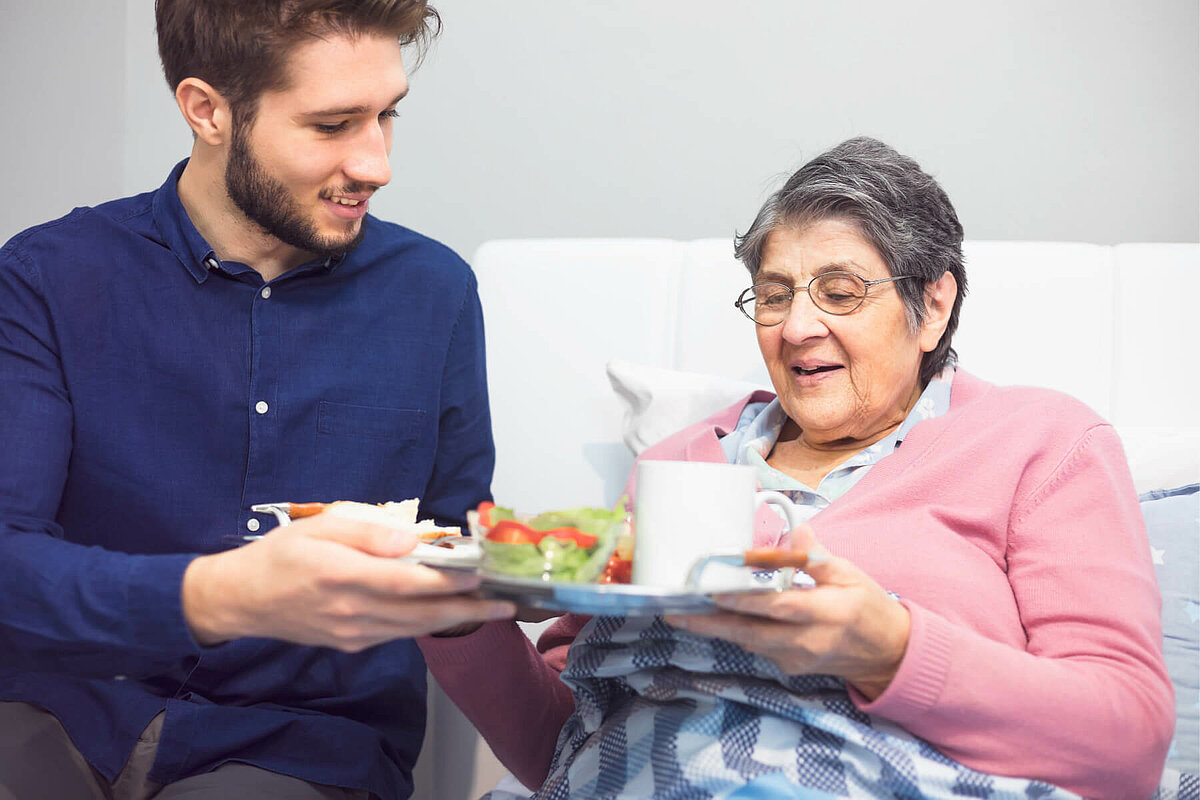 Mitarbeiter im FSJ reicht Senioren das Essen im Altenheim