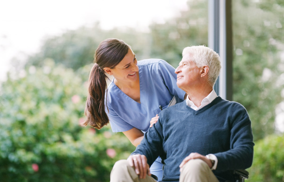 Pflegefachkraft bei Alloheim Senioren-Residenzen lächelt zu Senior im Rollstuhl